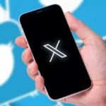 Une main tient un smartphone affichant le logo X